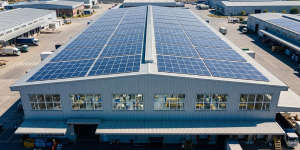 Commercial solar electric panels on a factory rooftop with workers operating inside during daytime production hours