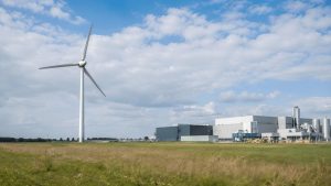 Open land beside a manufacturing facility with a wind turbine, representing site suitability for wind energy installation