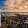 Commercial wind turbines operating alongside a large industrial manufacturing facility at dusk