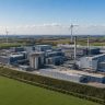 Wind turbines installed on open land adjacent to a large industrial factory complex
