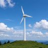 Small wind turbine on a green hilltop with blue sky and mountain range background